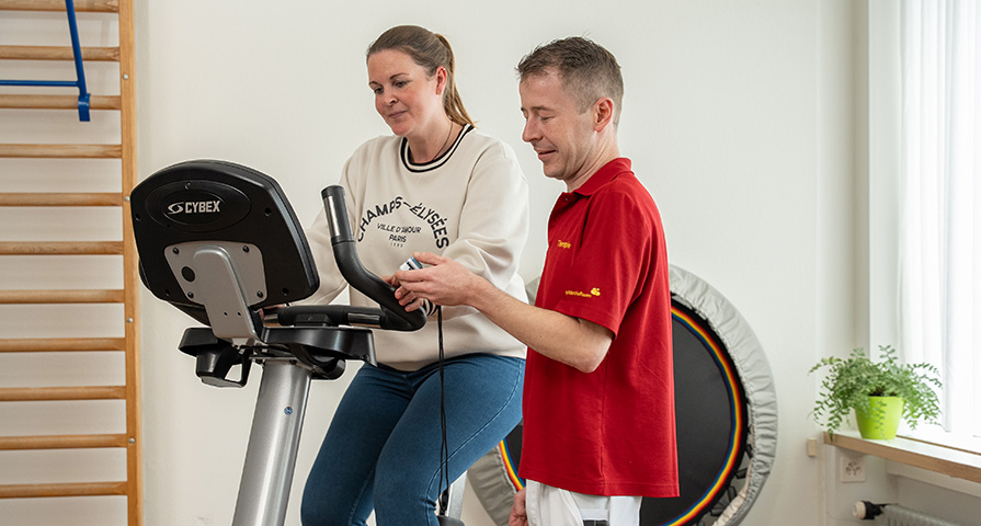 Eine Therapiefachpersonen erklärt einer Patientin ein Belastbarkeitstraining auf dem Ergometer, um die Lungenfunktion zu verbessern. 